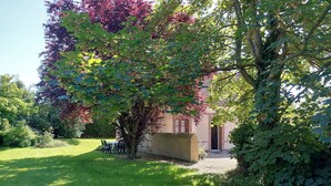 Un jardin avec un bâtiment en briques, un arbre aux feuilles rouges et une table avec des chaises.