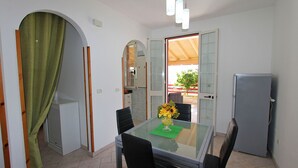 A dining area with a glass table, black chairs, a vase with flowers, and a refrigerator.