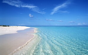 En strand med kristallklart, turkosfärgat vatten och vit sand.