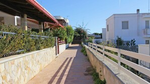 A paved pathway flanked by stone walls and white railings, leading to a building with a red roof.