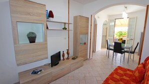 A modern living room with a sofa, TV, and shelves with decorative items.