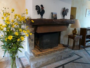 A fireplace with decorative roosters, a vase of yellow flowers, and a bookshelf in a room with tiled flooring. - Traditional Beauce cottage - 6 guests (Ardelu)