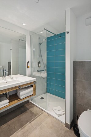 A modern bathroom with a glass-enclosed shower, a white sink with a wooden vanity, and a large mirror.