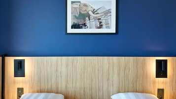 Ein Hotelzimmer mit blauer Wand, einem gerahmten Bild eines mechanischen Elefanten und einem hölzernen Kopfteil.