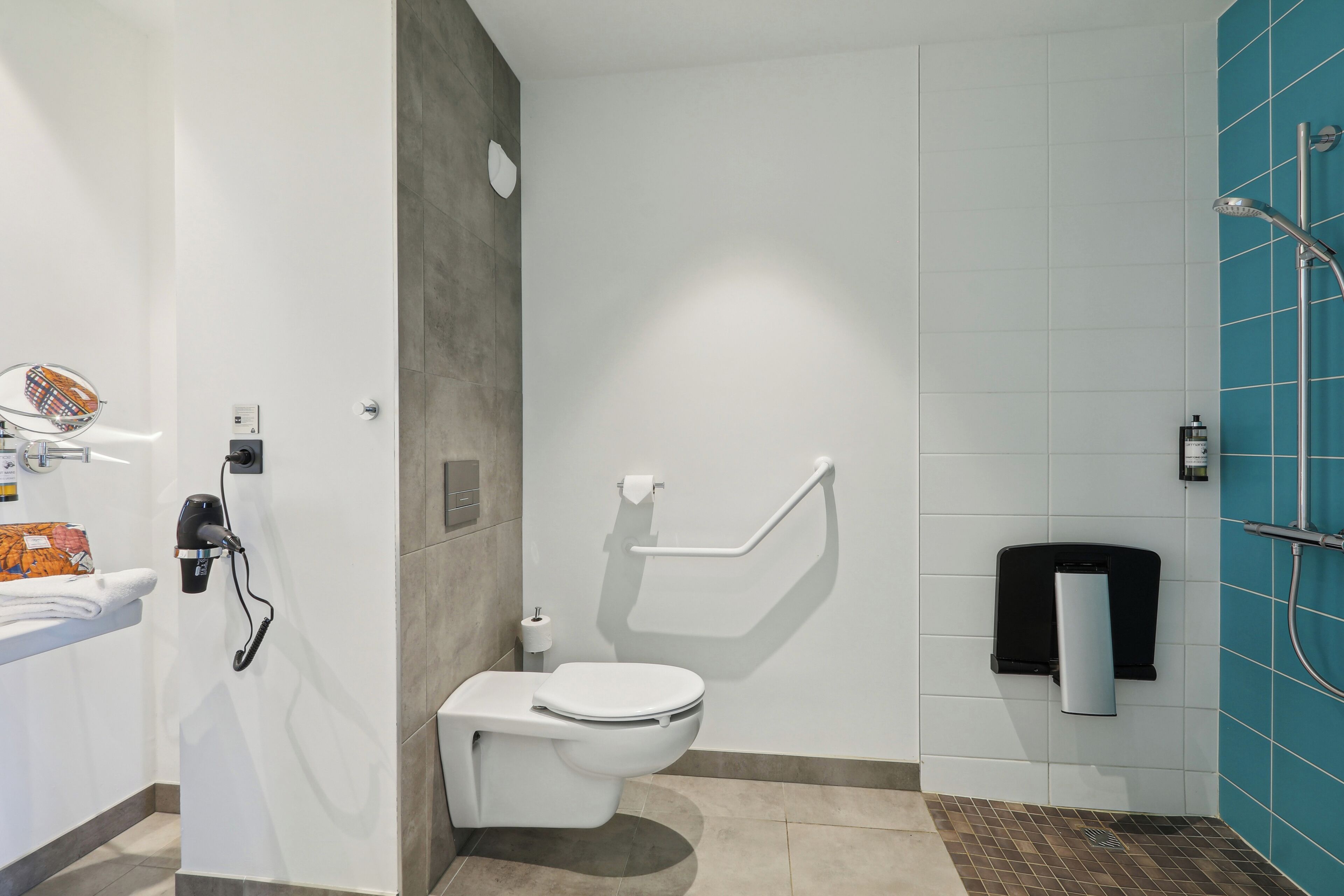 A modern bathroom with a white toilet, a towel rack, a hand dryer, and a shower area with a blue tiled wall.