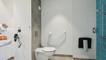A modern bathroom with a white toilet, a towel rack, a hand dryer, and a shower area with a blue tiled wall.