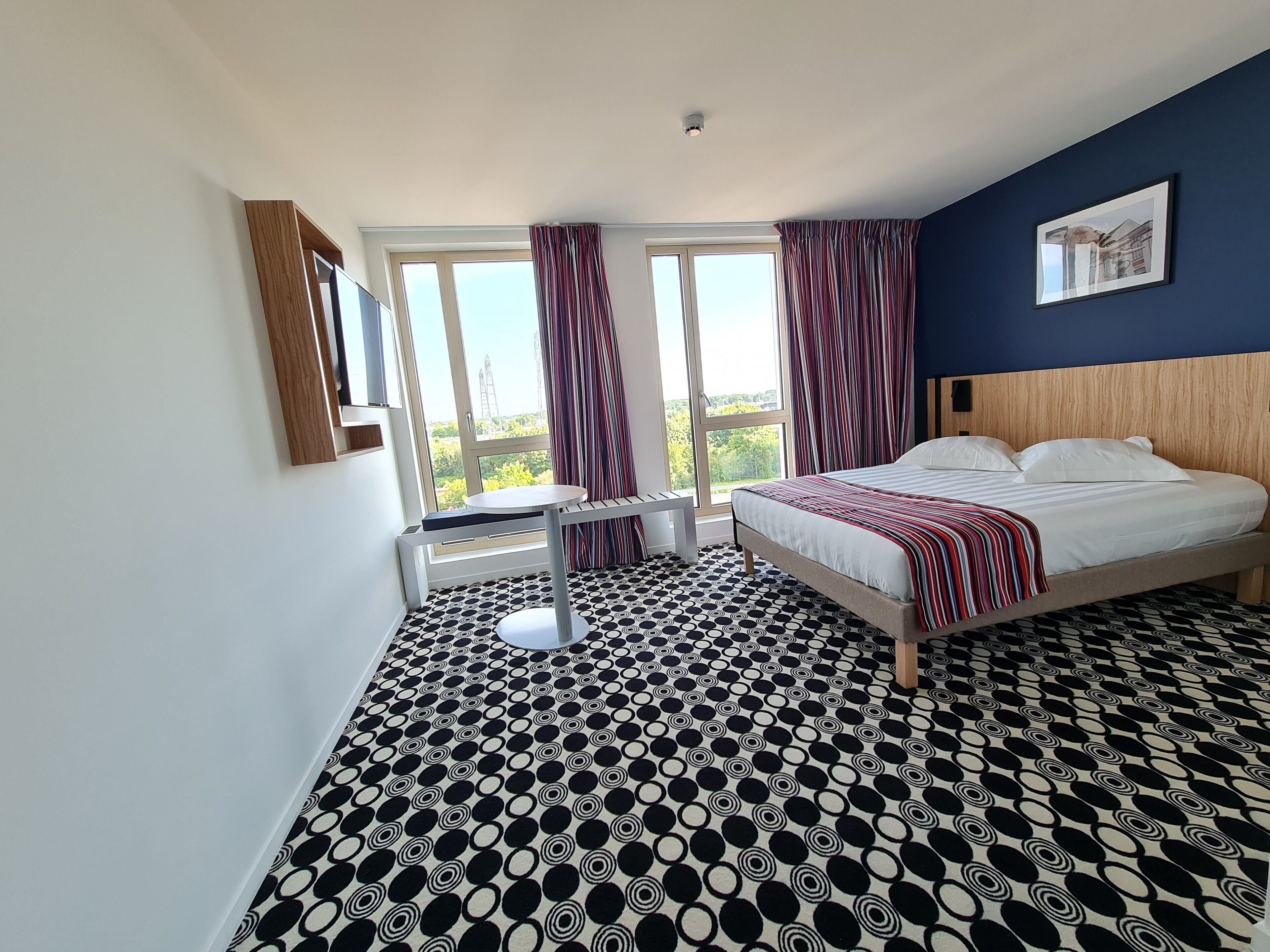 A hotel room with a bed, a small table, and a window with curtains.