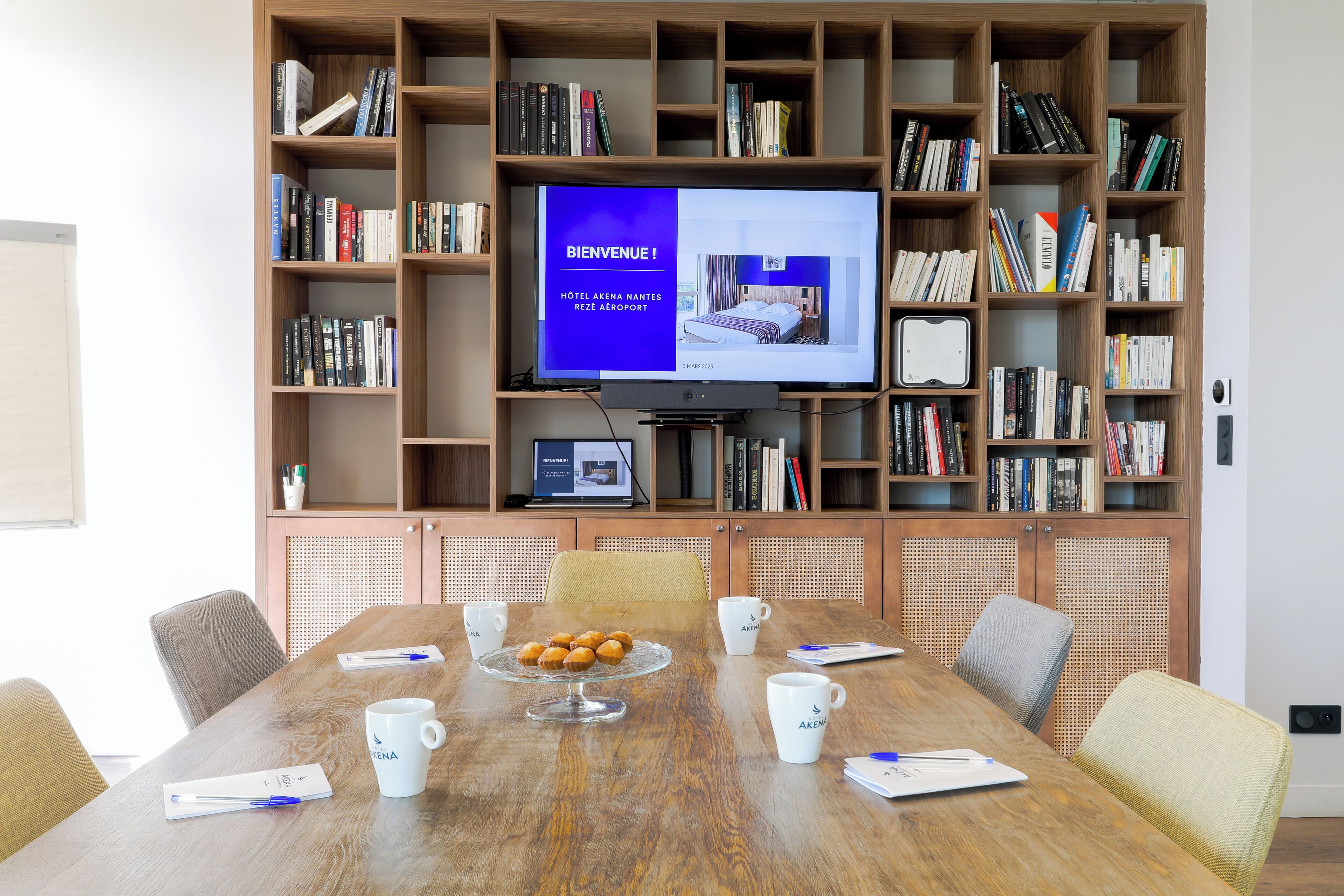 A conference room with a large table, chairs, a coffee station, and a bookshelf with books.