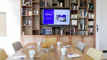 A conference room with a large table, chairs, a coffee station, and a bookshelf with books.