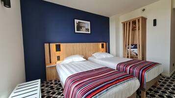 Habitación de hotel con dos camas, un armario de madera, un cuadro enmarcado en la pared y un piso con estampado.