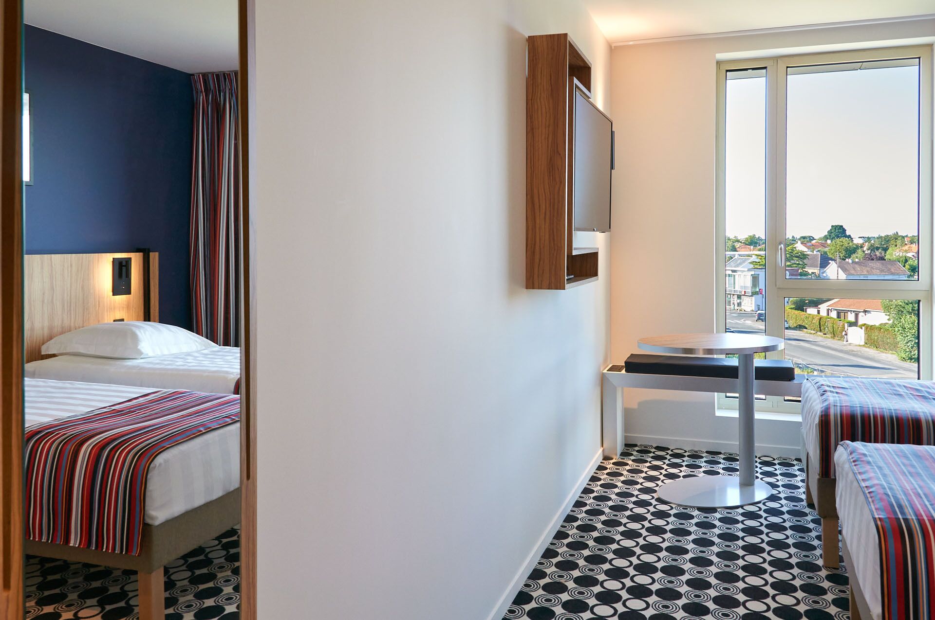 Une chambre d’hôtel équipée d’un lit, d’un bureau, d’une chaise, d’une télévision et d’une fenêtre donnant sur l’extérieur.