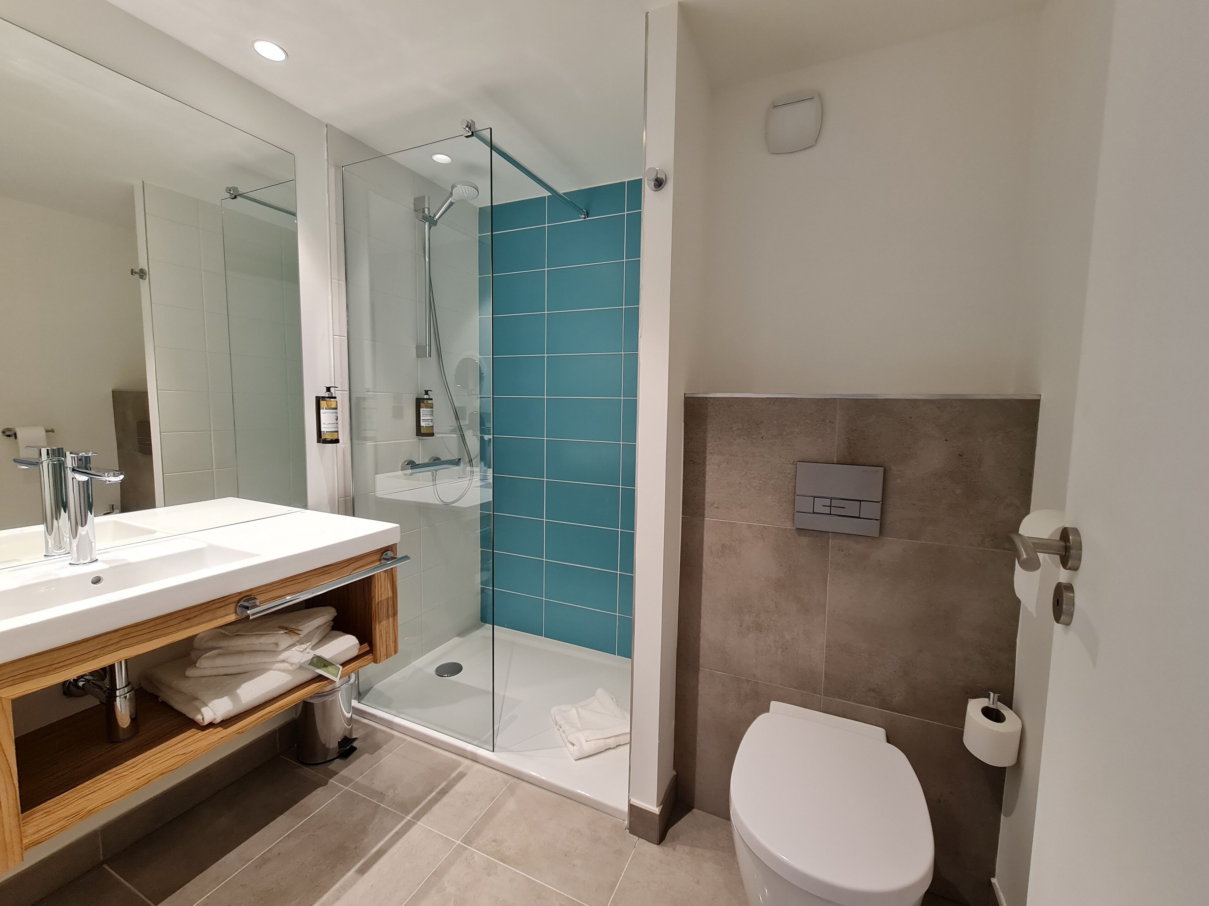 Un baño moderno con ducha envuelta en vidrio, un lavabo blanco con espejo y un inodoro.