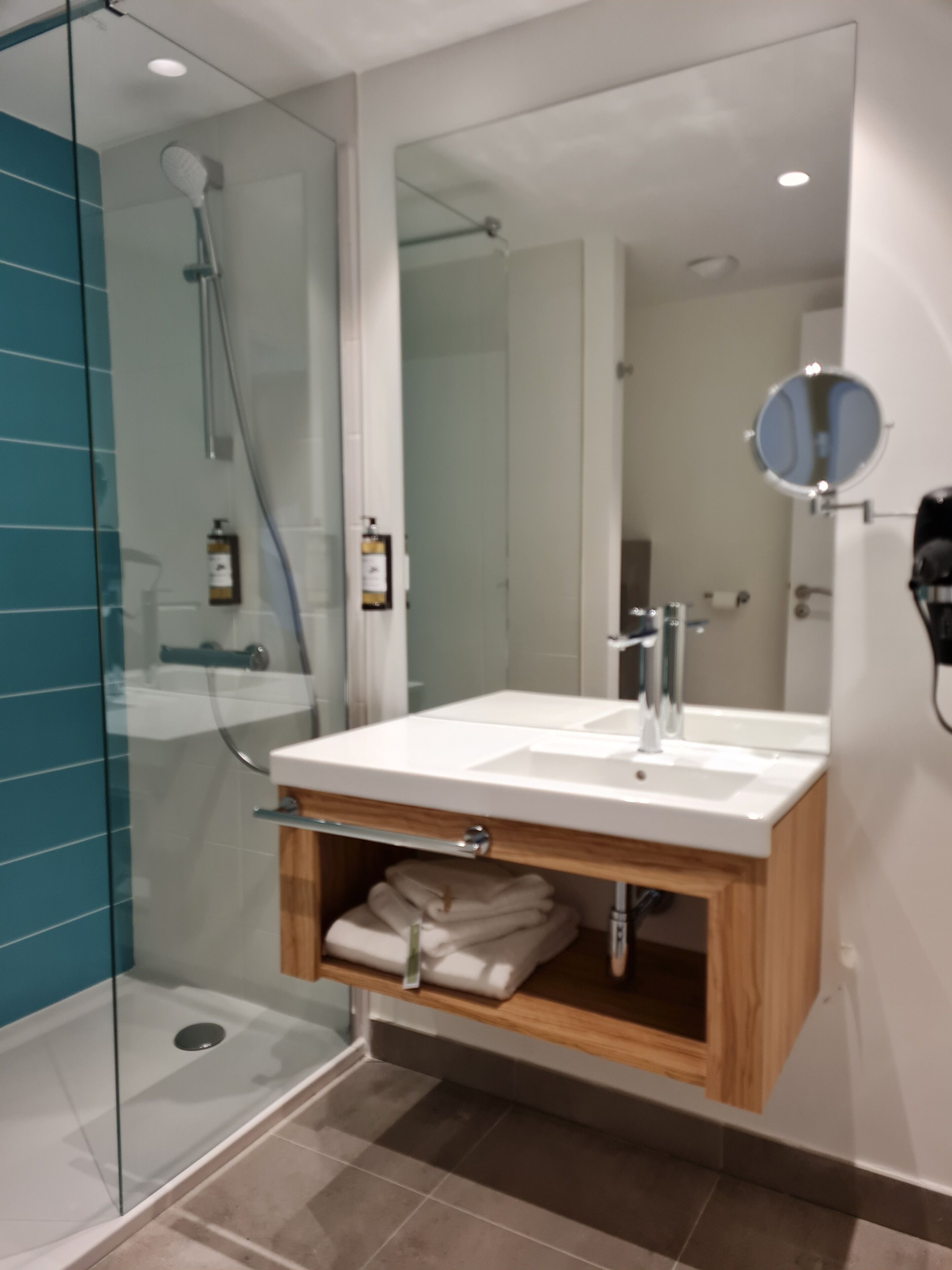 Un baño moderno con cabina de ducha de vidrio, un lavabo blanco con mueble de madera debajo y un espejo encima.