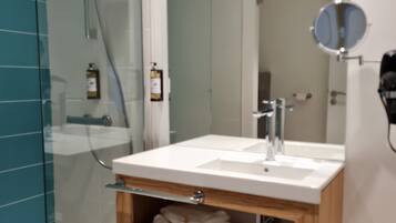 Un baño moderno con cabina de ducha de vidrio, un lavabo blanco con mueble de madera debajo y un espejo encima.