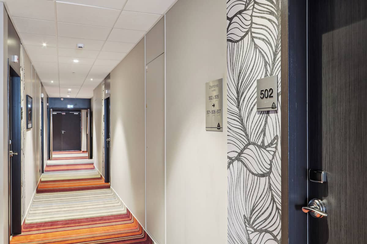 A hotel corridor with a striped carpet, a door labeled '502', and a wall with a leaf pattern.