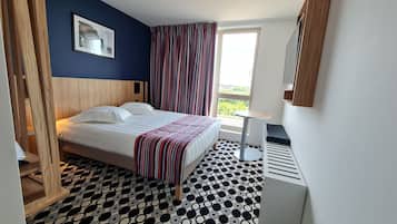 Una camera d'albergo con un letto, un tavolino, una finestra con tende e un pavimento decorato.