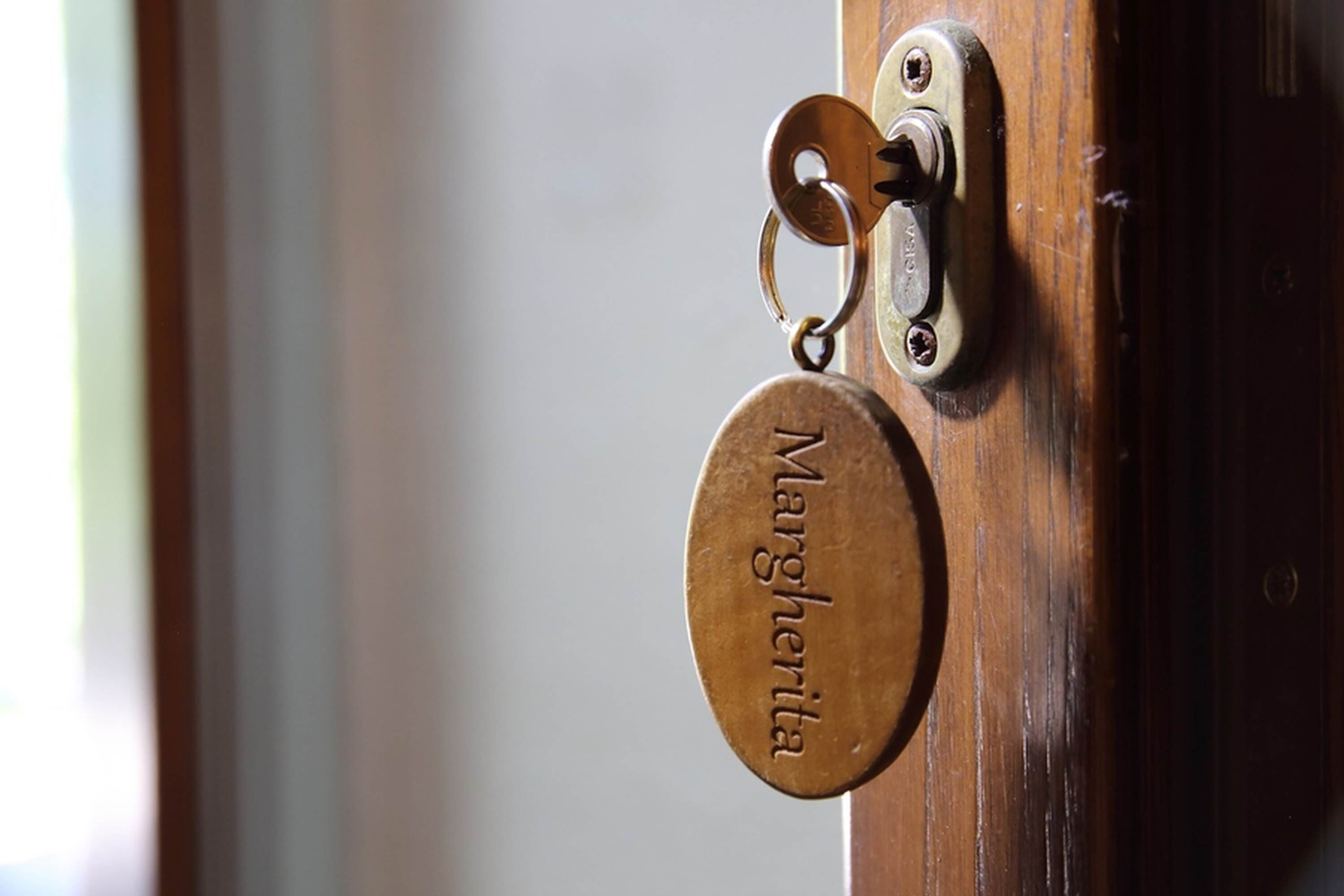 A door with a metal keyhole and a brass keychain with the name "Margherita" engraved on it.