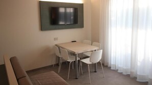 A modern dining area with a table and chairs, a flat-screen TV mounted on the wall, and sheer curtains on the window. - Persea Mare 5A tutti i comfort a 2 passi dal mare (Arma di Taggia)