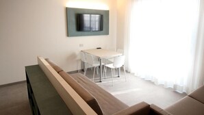 A modern hotel room with a flat-screen TV mounted on the wall, a dining table with four chairs, and a sofa with a bench. - Persea Mare 5A tutti i comfort a 2 passi dal mare (Arma di Taggia)