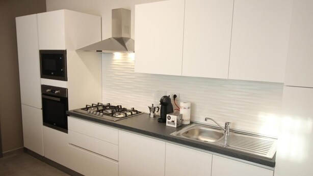 A modern kitchen with white cabinetry, a gas stove, a sink, and built-in ovens. - Persea Mare 5A tutti i comfort a 2 passi dal mare (Arma di Taggia)
