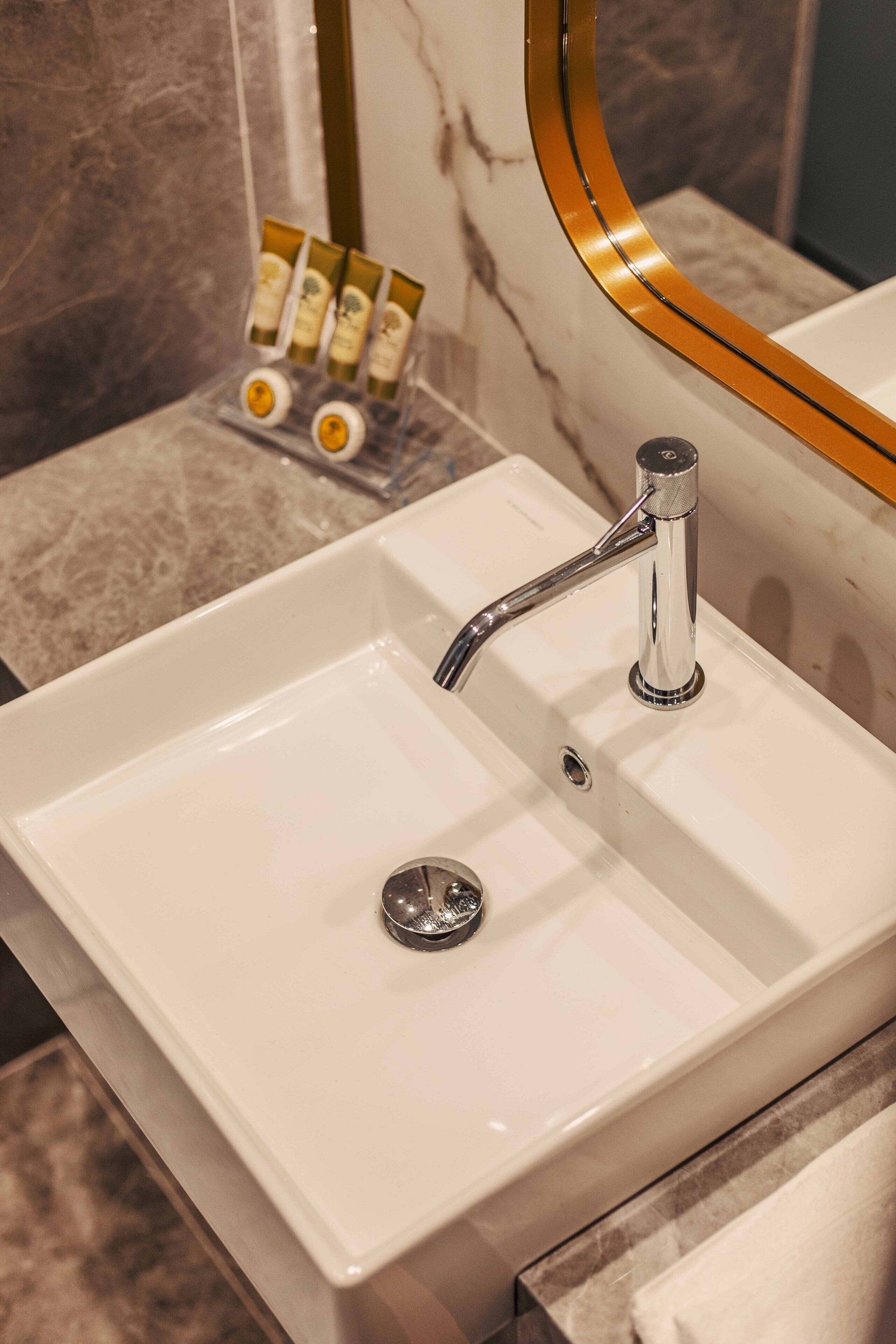 Un lavabo de baño con grifo cromado, un espejo con marco dorado y una pared de mármol.