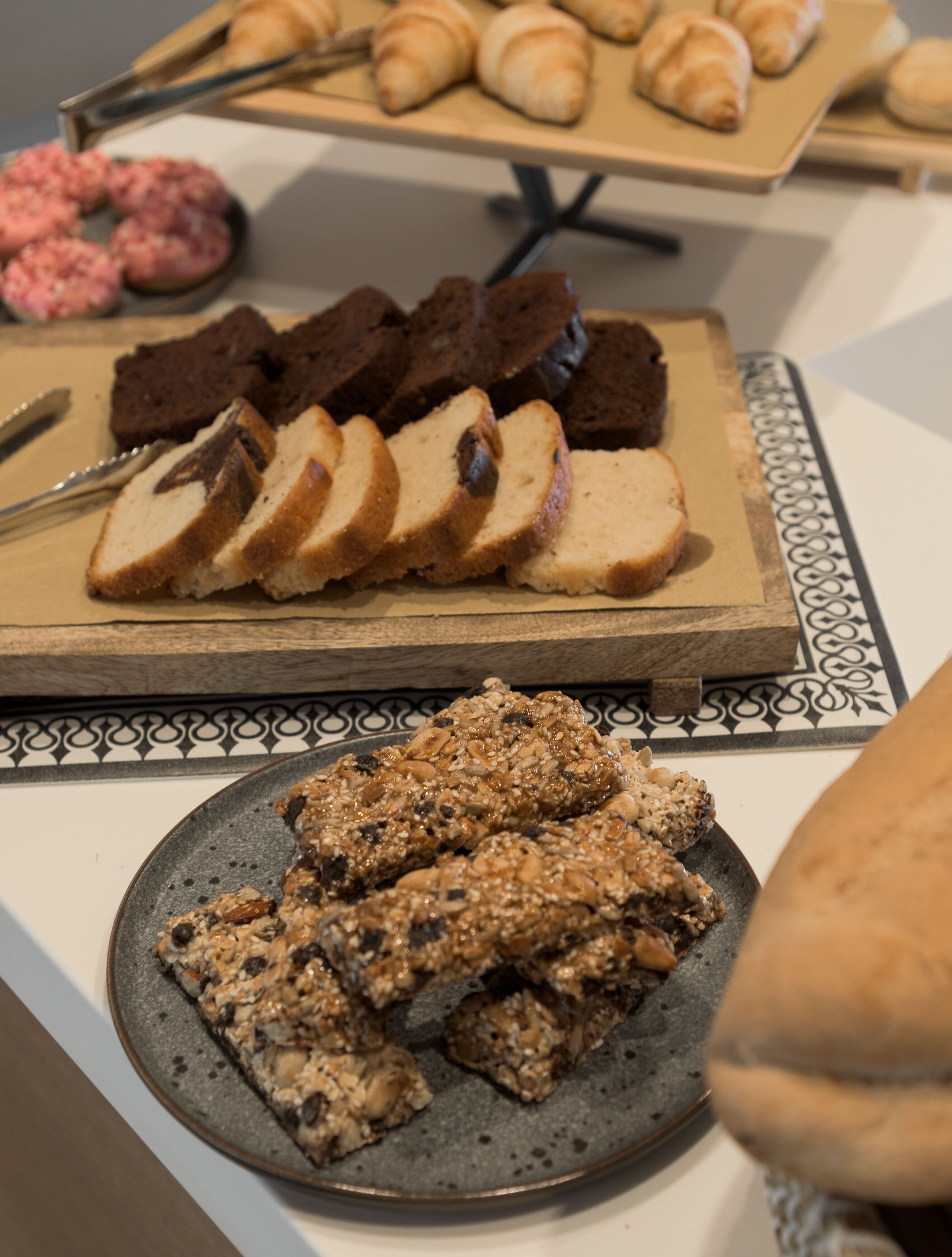 Une table sur laquelle on trouve divers aliments, notamment du pain, des pâtisseries et une assiette de granola.