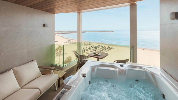 A balcony with a sofa and a hot tub overlooking a beach. - Bio Beach Boutique Hotel (Rethymno)