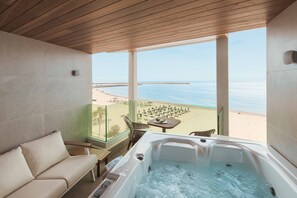 A balcony with a sofa and a hot tub overlooking a beach. - Bio Beach Boutique Hotel (Rethymno)