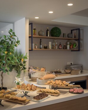 A buffet with various baked goods and pastries, a toaster, and shelves with bottles and decorative items. - Bio Beach Boutique Hotel (Rethymno)