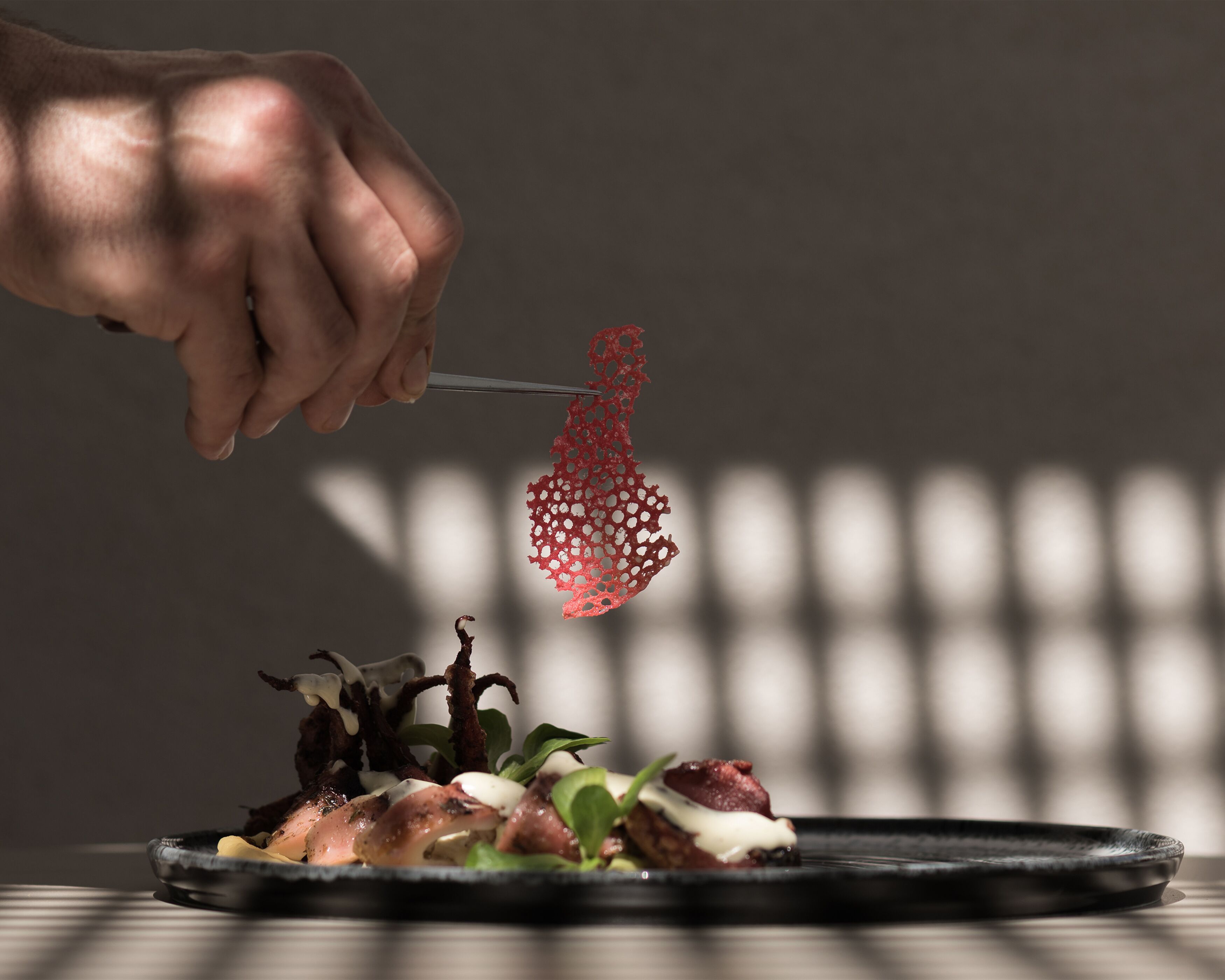 A hand holding a fork with a red, intricate food item above a plate of food.