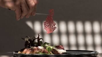 A hand holding a fork with a red, intricate food item above a plate of food.
