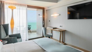 A hotel room with a bed, a desk, a chair, a TV, and a view of the ocean. - Bio Beach Boutique Hotel (Rethymno)