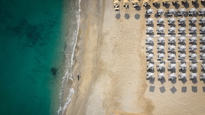 An aerial view of a beach with rows of umbrellas and sun loungers, a sandy shore, and a clear blue sea. - Bio Beach Boutique Hotel (Rethymno)