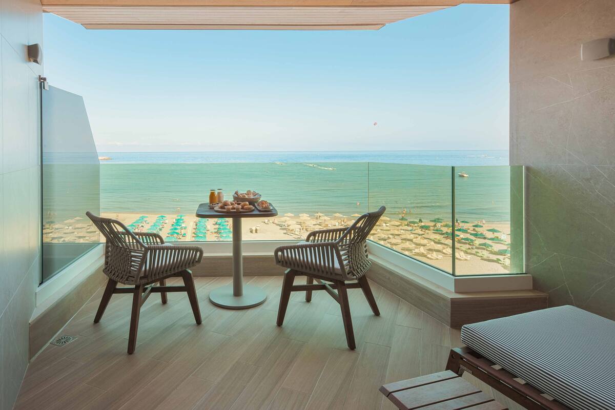 A balcony with a view of the beach, two wicker chairs, a small table with drinks, and a sofa.