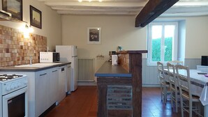 Cuina amb fogó de gas, armaris blancs, rebedor de rajola, sostre amb bigues de fusta i zona de dinar amb taula i cadires.