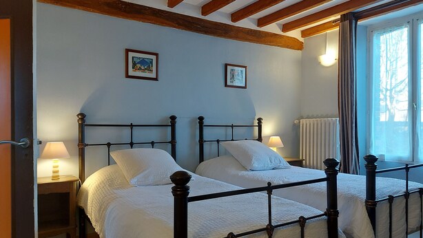Un dormitori amb dos llits, bigues de fusta al sostre, una finestra amb cortines i dues làmpades de nit.