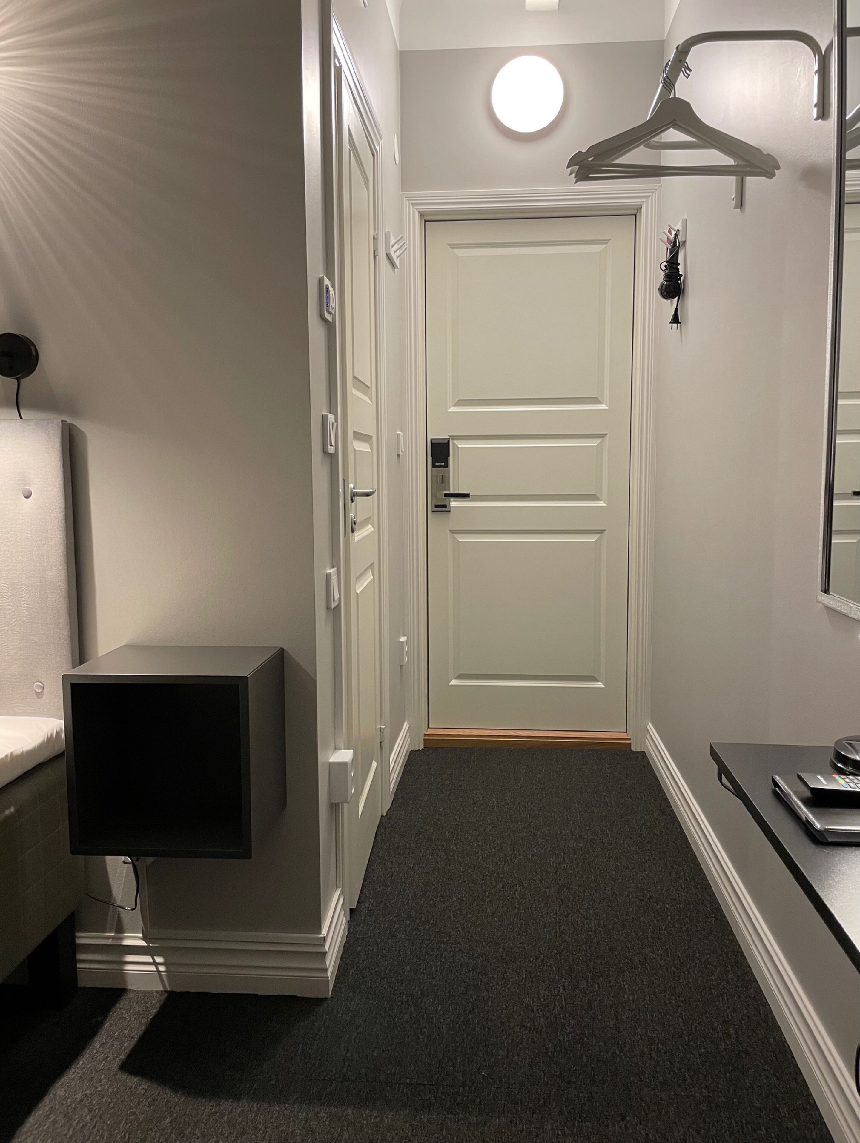 Een hal met een witte deur, een kapstok, een klein tafeltje met een weegschaal en een wandlamp.