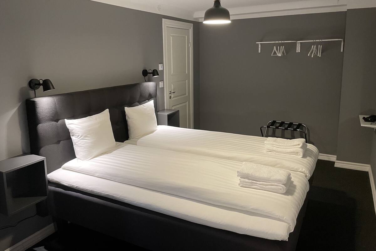 Una cama bien tendida con sábanas blancas, un cabecero negro y dos lámparas de noche.