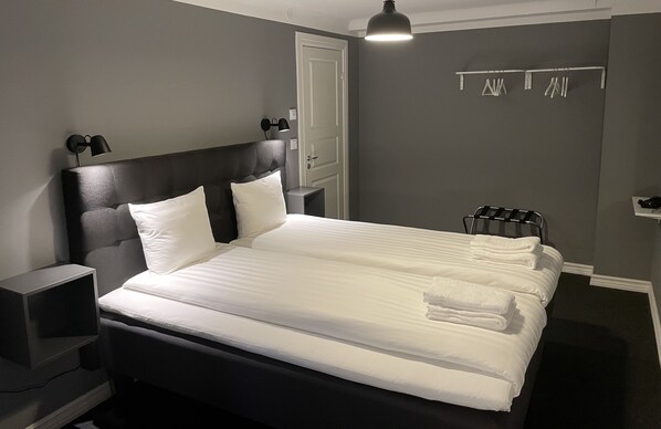 A neatly made bed with white linens, a black headboard, and two bedside lamps. - Unique Hotel Jungfrugatan (Stockholm)