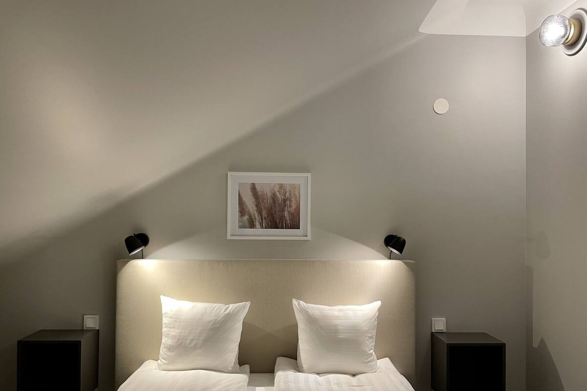 Un dormitorio con una cama, dos mesitas de noche, un cuadro en la pared y dos lámparas de pared.