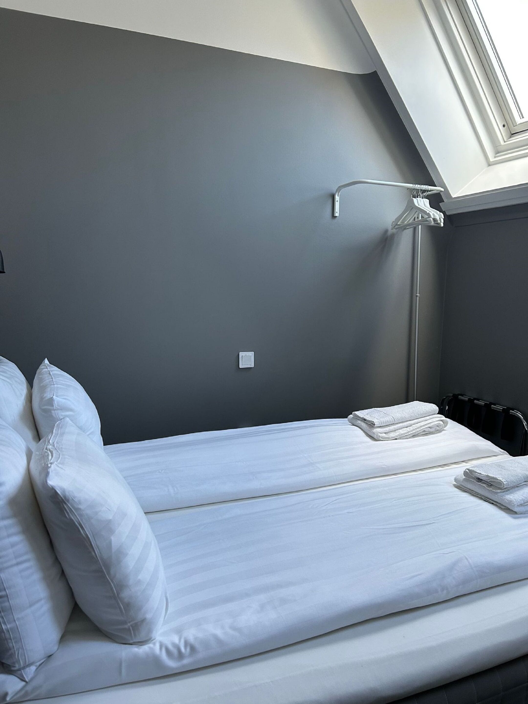 A single bed with white linens and pillows, a ceiling light, and a radiator.