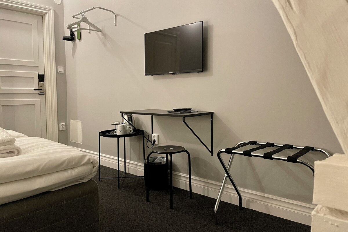 A hotel room with a bed, a desk with a chair, a TV mounted on the wall, and a wall-mounted towel rack.