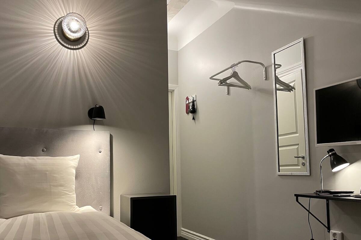 Una habitación de hotel con cama, lámpara de noche, espejo en la pared y televisor.