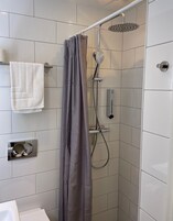 Un área de ducha con cortina gris, ducha de mano y panel de control en la pared.