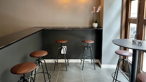 En modern bardisk med tre barstolar, ett runt bord, hängande lampor och en orkidé i en kruka.