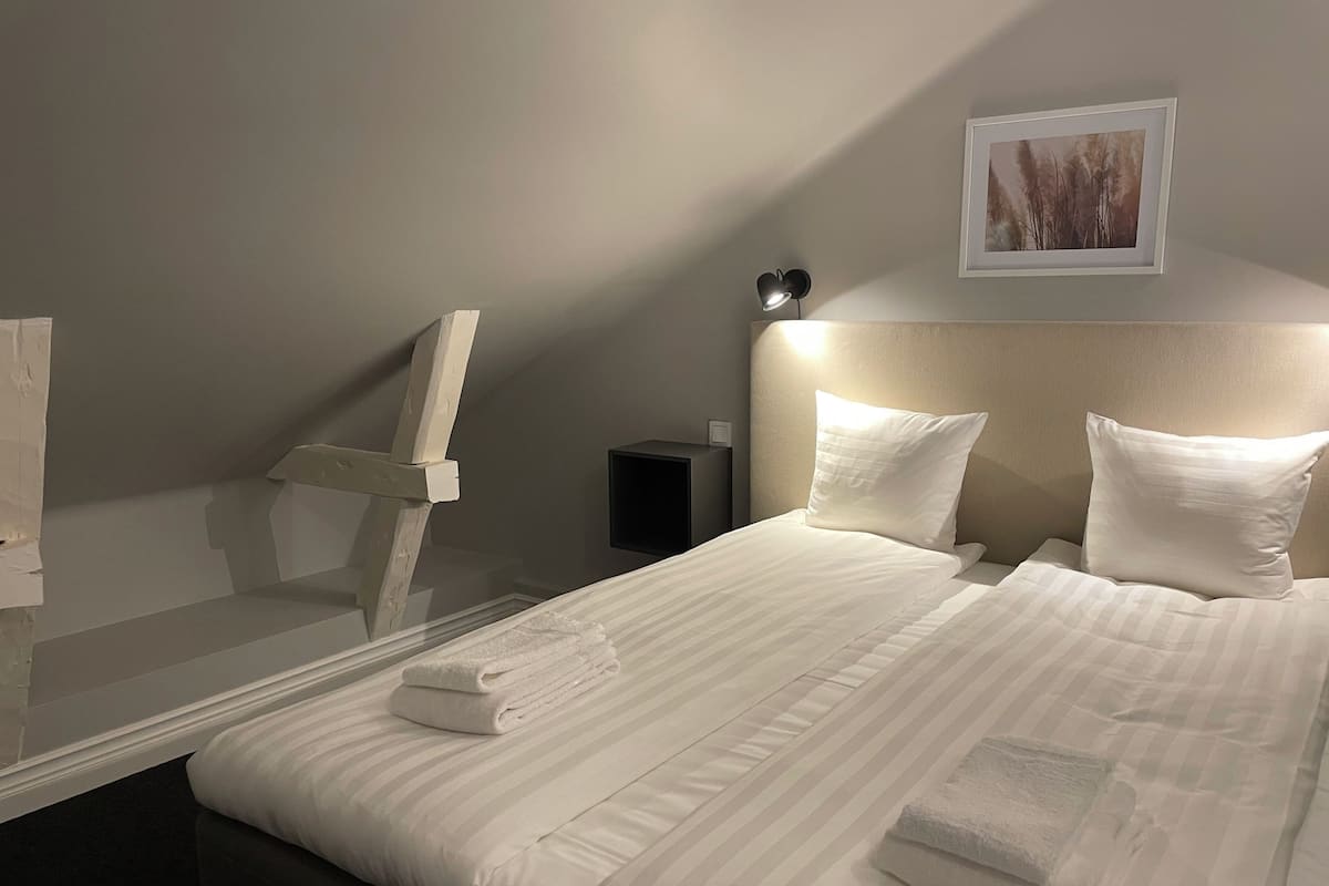 A neatly made bed with white linens, a headboard with integrated lighting, a framed picture on the wall, and a small bedside table with a lamp.