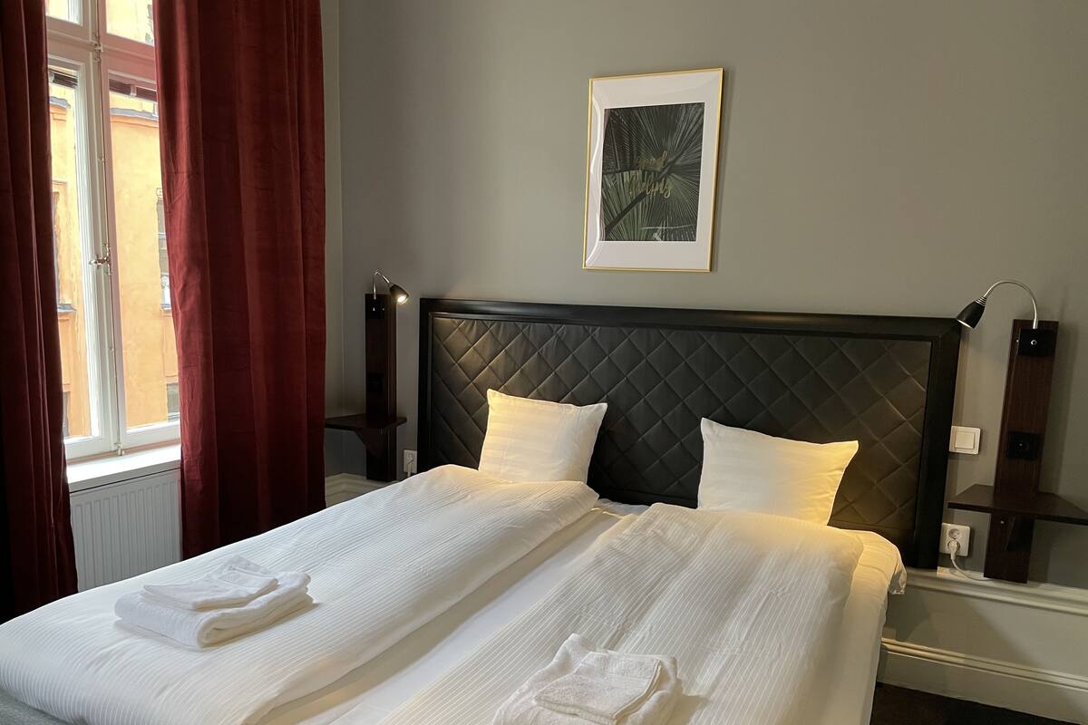 Una cama bien hecha con ropa y toallas blancas, un cabecero oscuro y un cuadro en la pared.