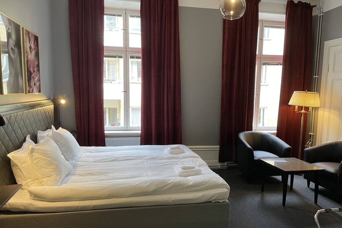 Una habitación de hotel con una cama grande, dos sillas, una mesa y una lámpara.