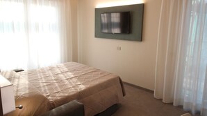 A hotel room with a bed, a flat-screen TV mounted on the wall, and a window with sheer curtains. - Persea Mare 5B tutti i comfort a 2 passi dal mare (Arma di Taggia)