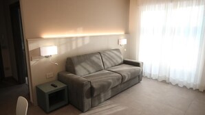 A modern hotel room with a grey sofa, a small bedside table, and a lamp. - Persea Mare 5B tutti i comfort a 2 passi dal mare (Arma di Taggia)